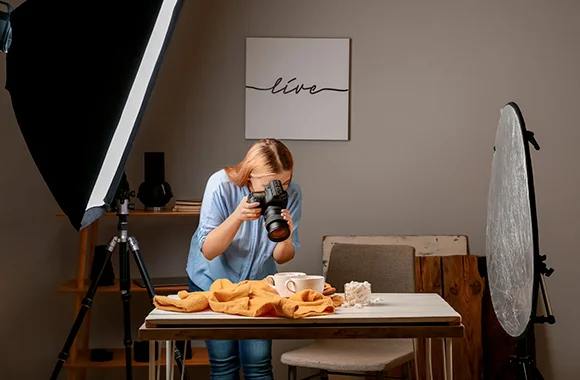 Une photographe cadre une table de nourriture entre une softbox et un réflecteur